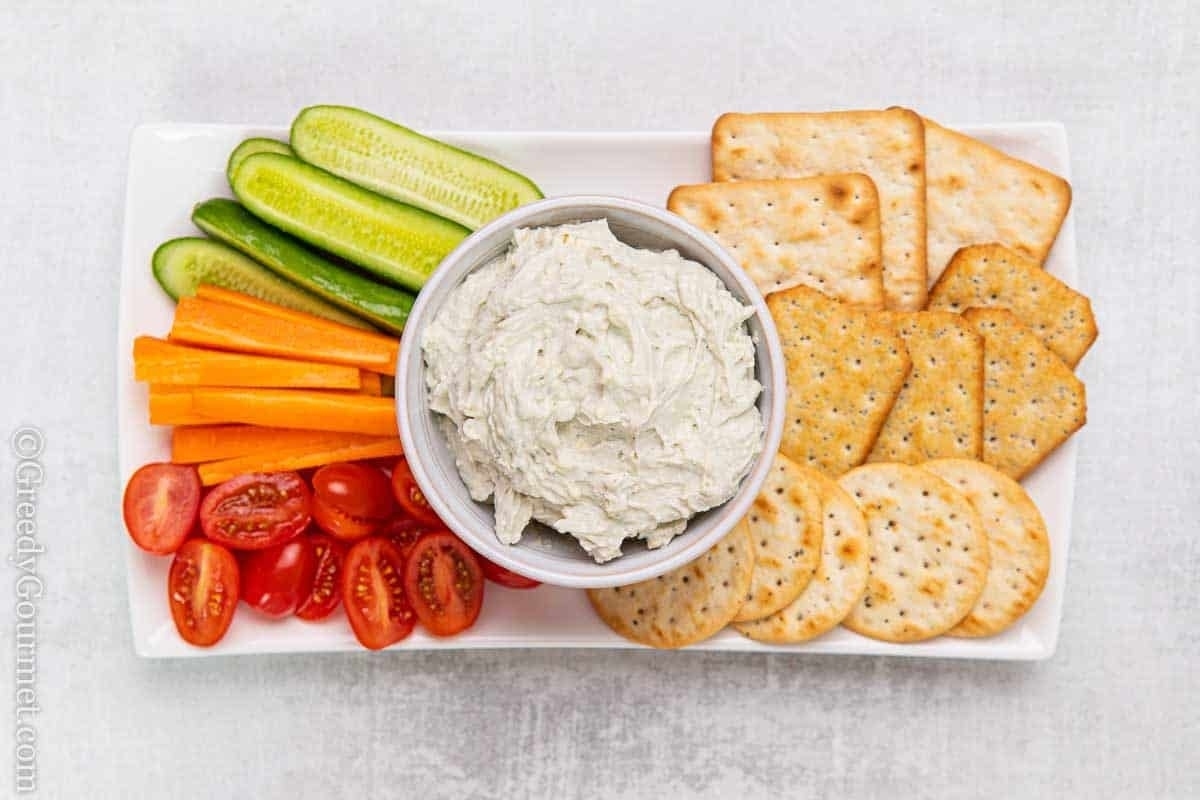 A plate with crackers, dip and vegetables featuring creamy cream cheese dip.