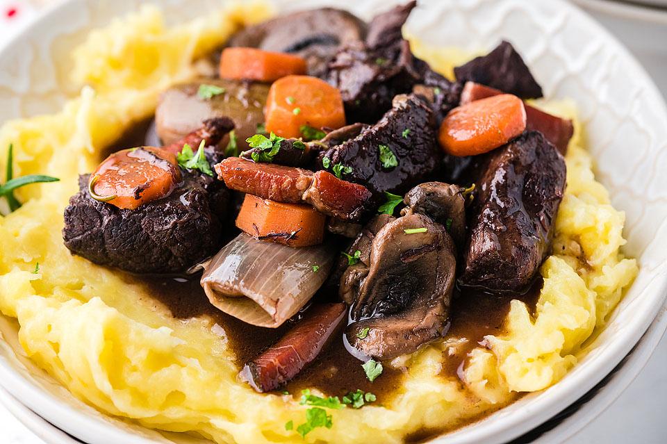 A hearty stew featuring carrots, mushrooms, and a creamy bed of mashed potatoes.