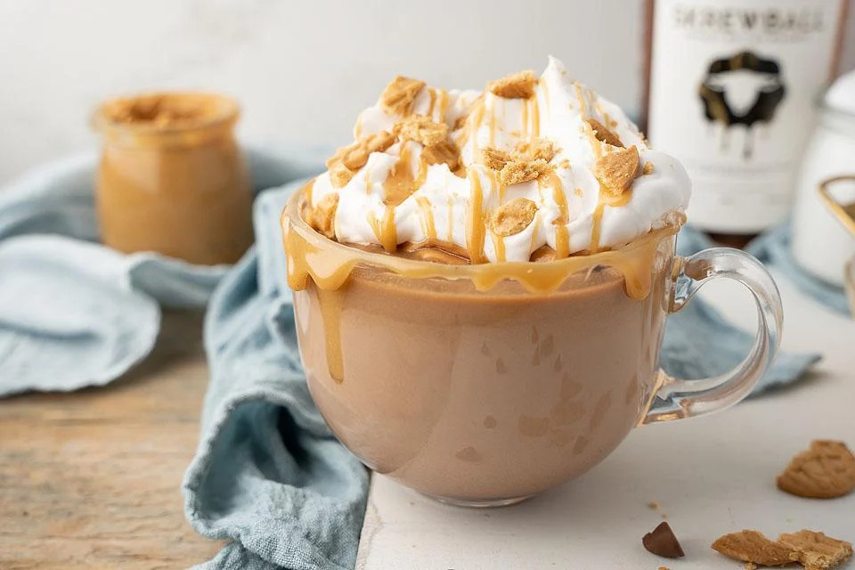 A mug of hot chocolate topped with whipped cream and a bottle of bourbon.