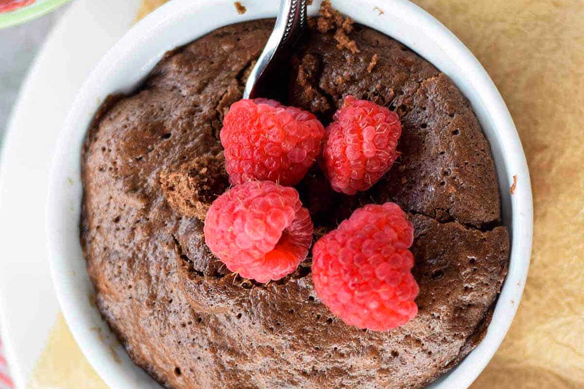 Chocolate pudding in a white bowl topped with raspberries.