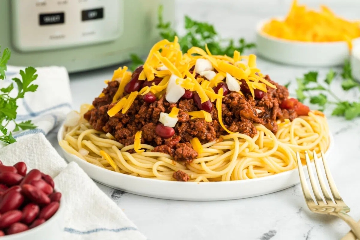 A plate of spaghetti and chili in front of an instant pot.