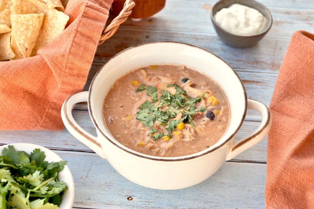 A flavorful bowl of slow cooker mexican chicken soup topped with crispy tortilla chips and a dollop of creamy sour cream.