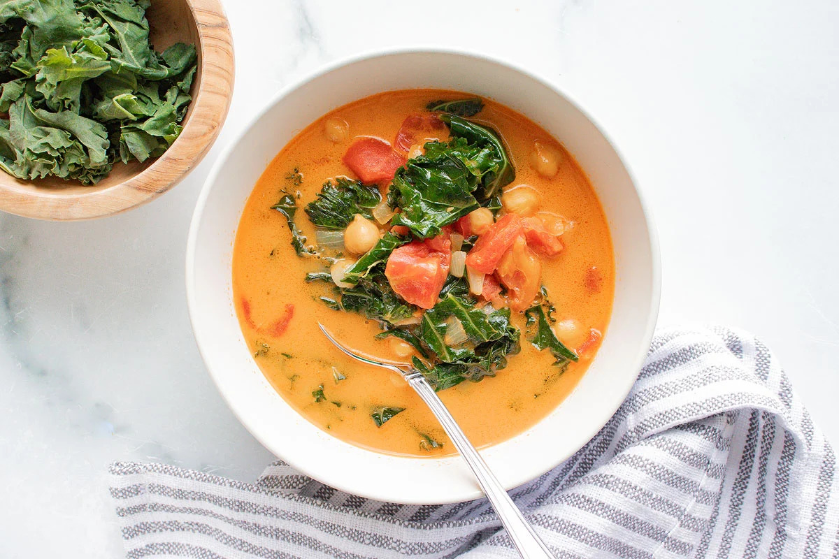 A bowl of tomato and kale soup with a spoon.