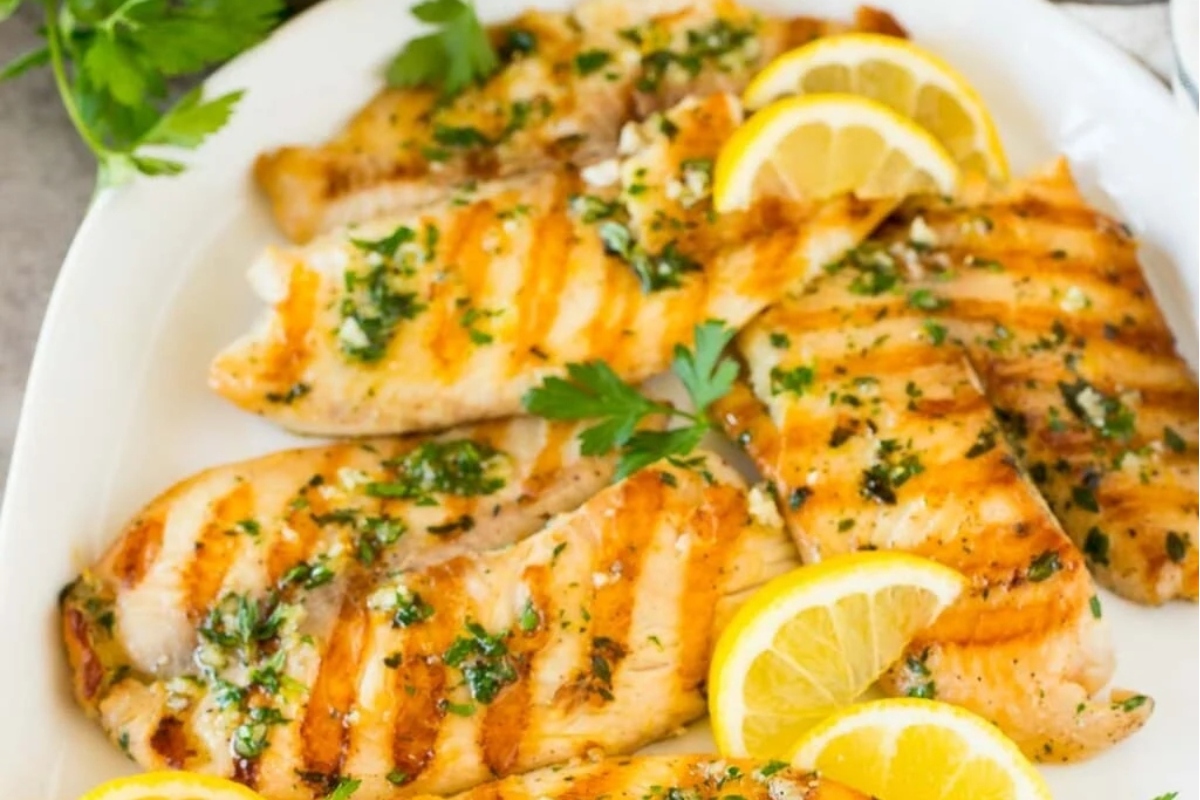 Delicious grilled fish with lemon and parsley on a pristine white plate.