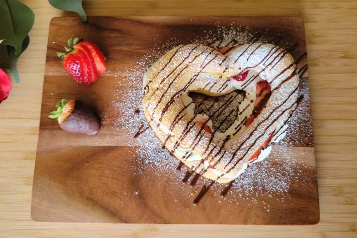 A heart shaped pastry with strawberries and chocolate on a wooden cutting board, perfect for Valentines' Day desserts.
