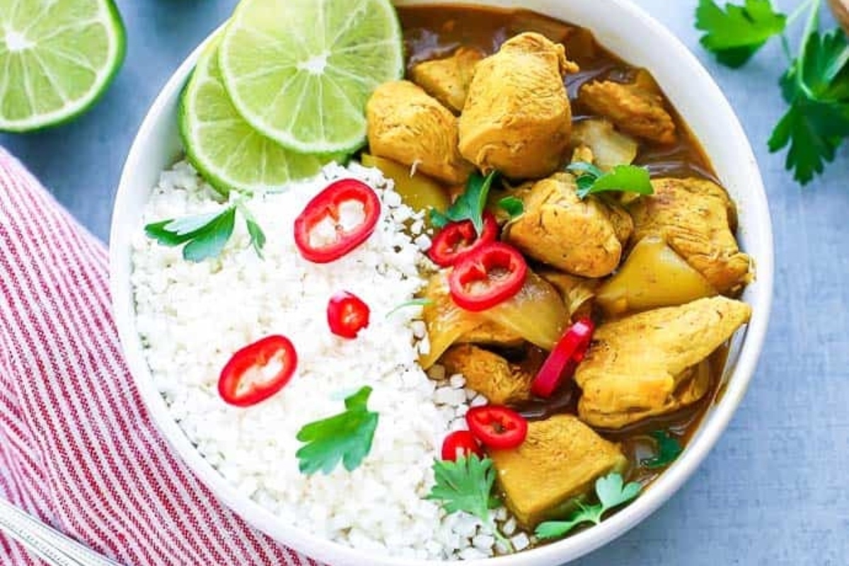 A flavorful dinner of chicken curry served with rice and garnished with lime wedges.