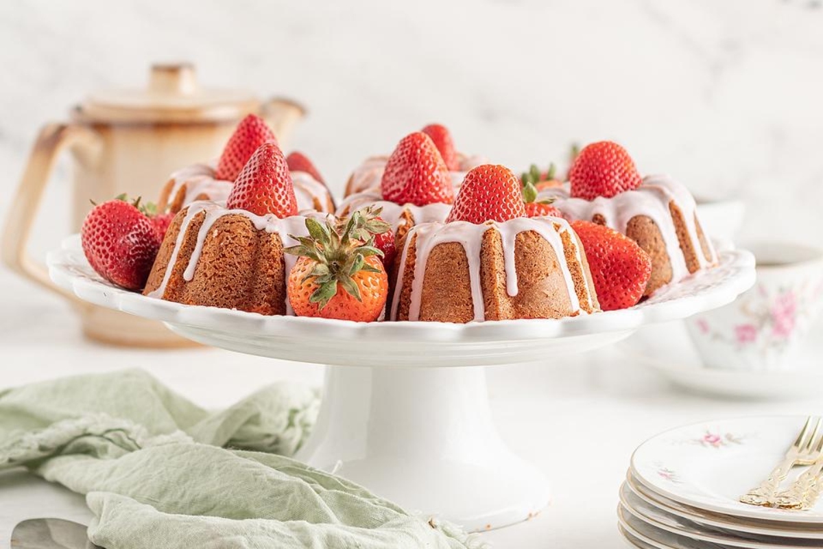 A bundt cake with strawberries and icing on a white plate.