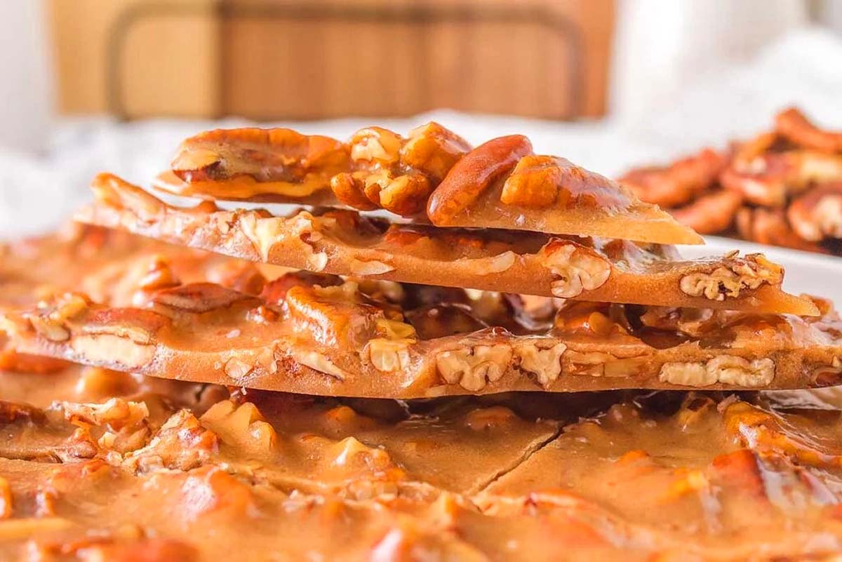 A stack of caramel pecan brittle, perfect for Christmas candy recipes, on a white plate.