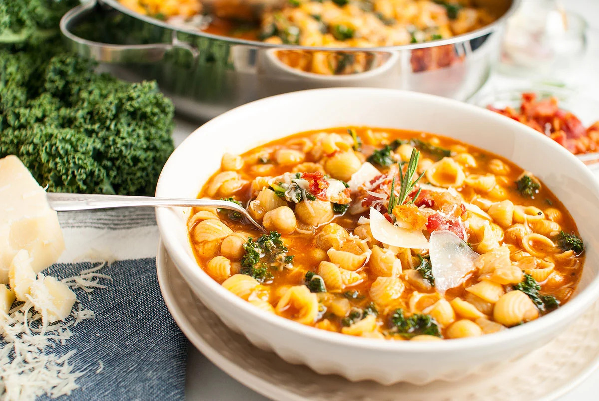 A comforting bowl of pasta and kale stew with a spoon.