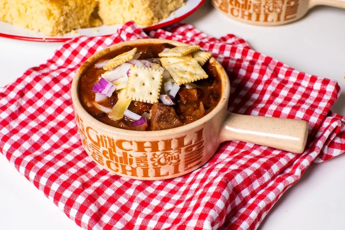 Chili in a slow cooker with cornbread on a table.