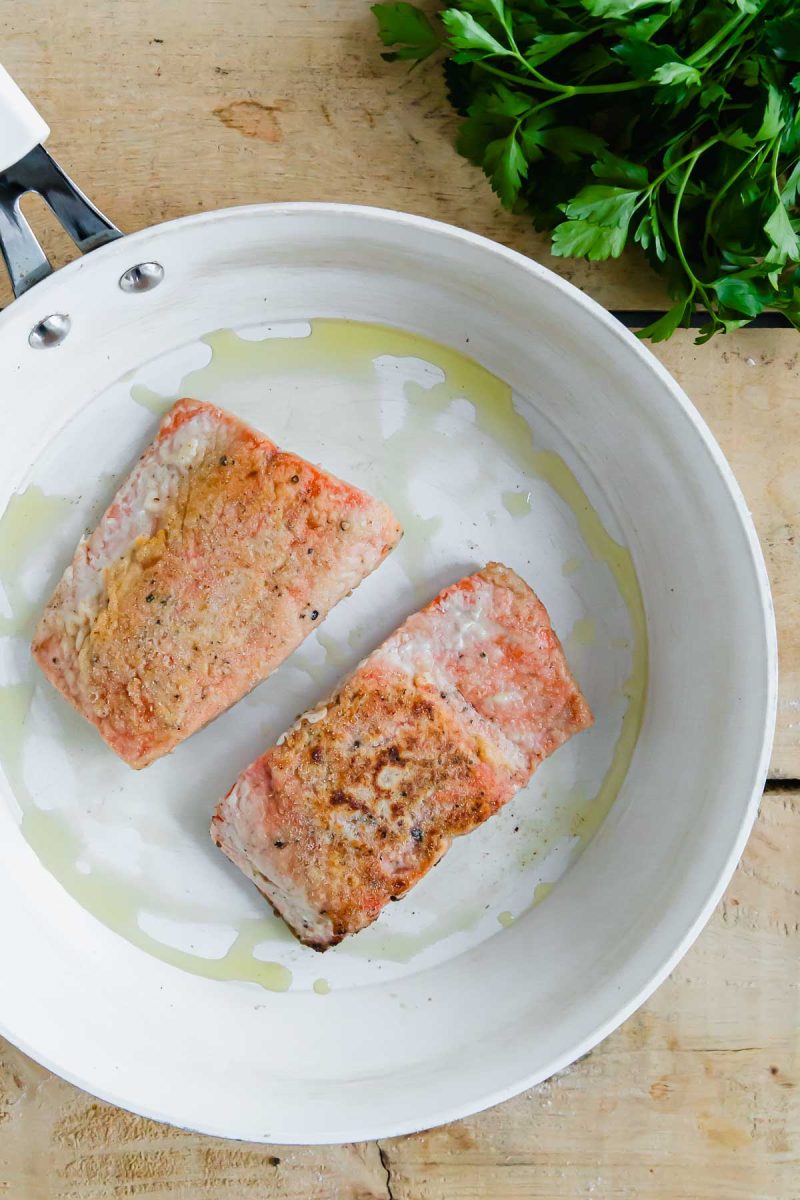 Two salmon fillets cooked in a pan on a wooden table.