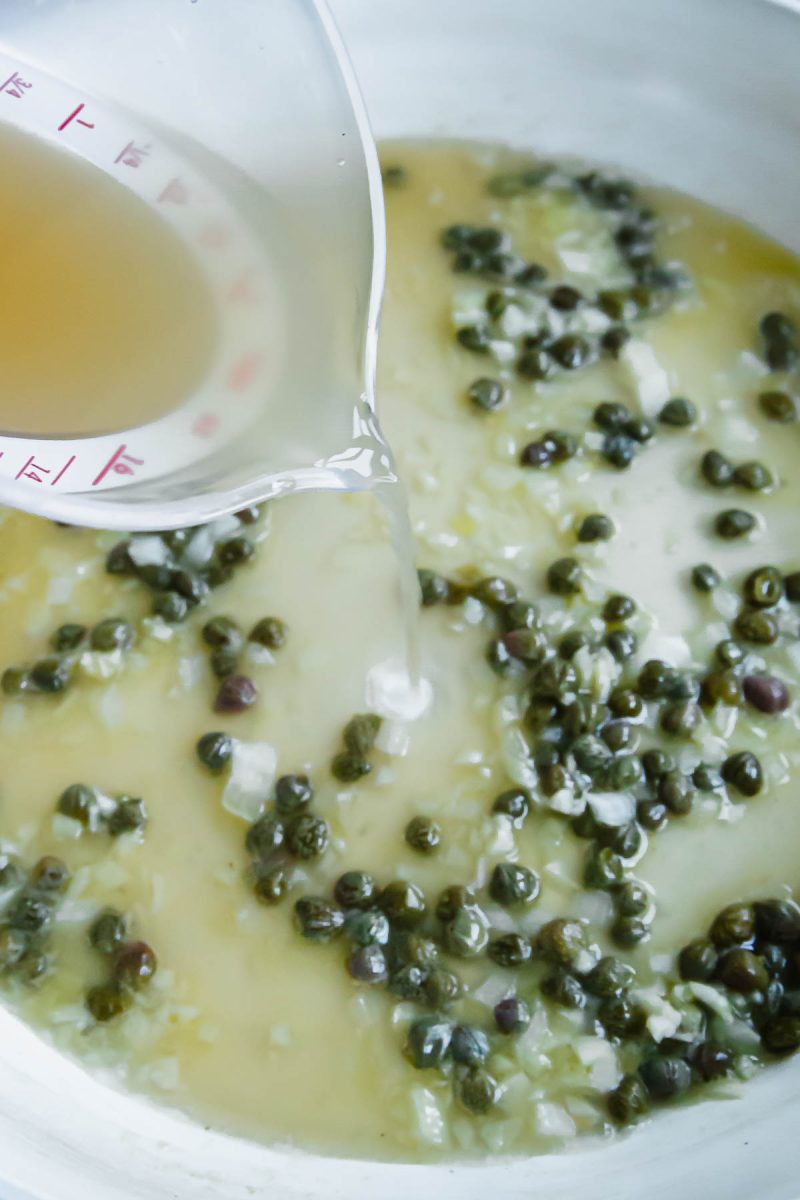 A liquid is being poured into a bowl of capers for salmon piccata.