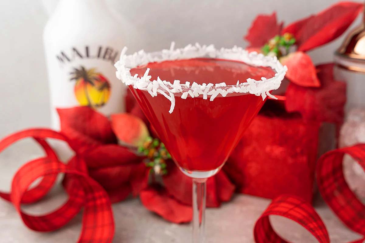 A festive martini glass filled with a vibrant red drink adorned with whimsical red ribbons evoking the spirit of Christmas cocktails.