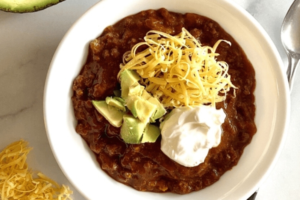 A tantalizing bowl of slow cooker chili served with creamy sour cream and topped with fresh avocado.