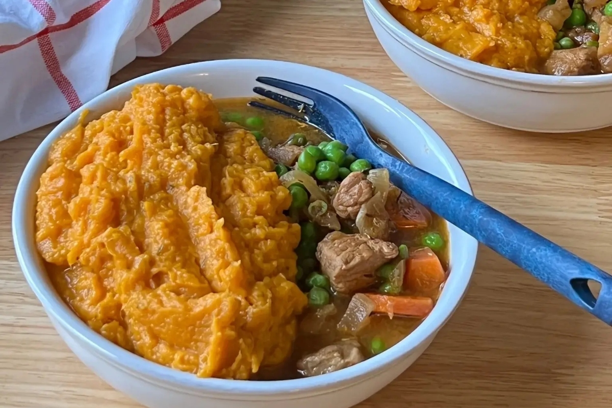 Two bowls of mashed potatoes and peas served alongside a hearty stew on a wooden table.