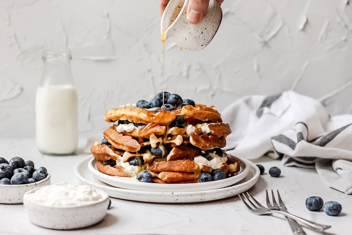 A stack of blueberry pancakes with whipped cream and blueberries.