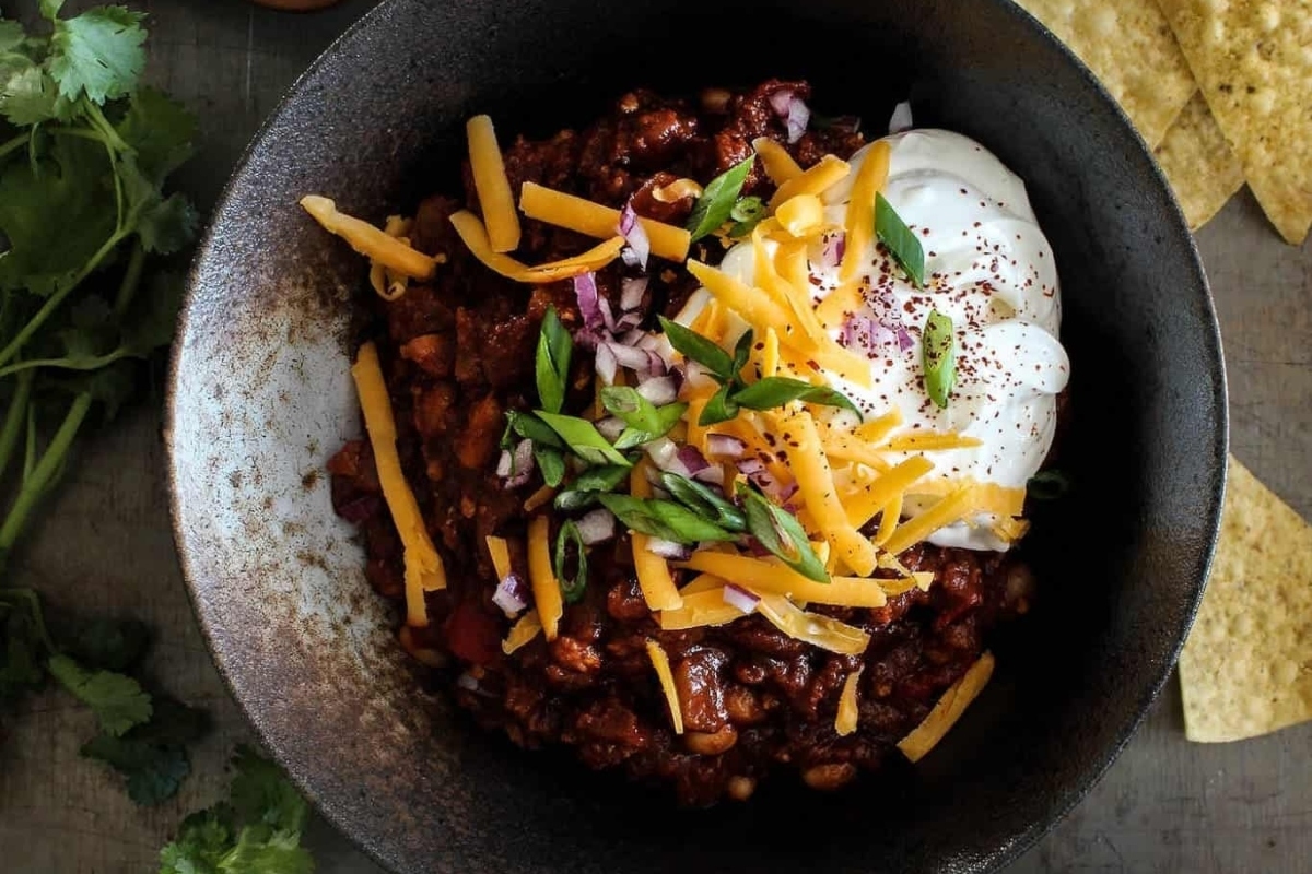 Slow cooker chili recipe in a bowl with sour cream and tortilla chips.