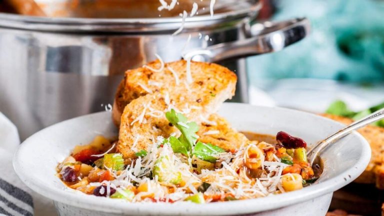 Italian minestrone soup in a while bowl with shredded cheese and toast.