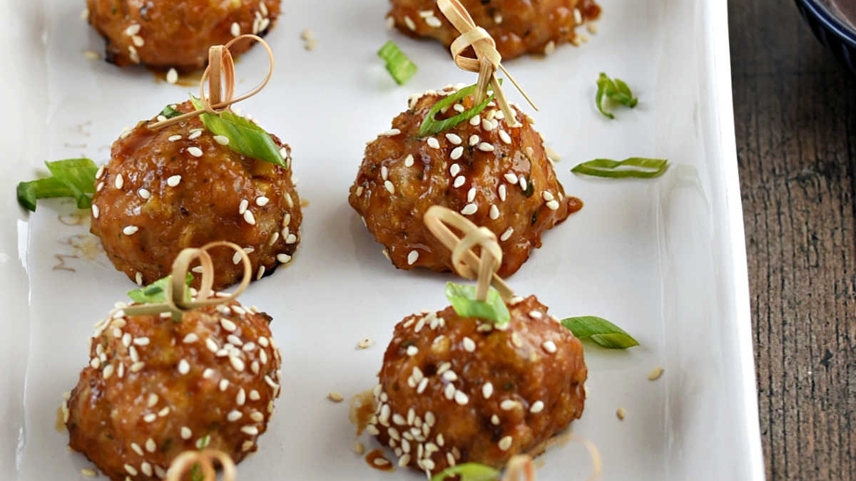 Asian meatballs on a white plate with sesame seeds.