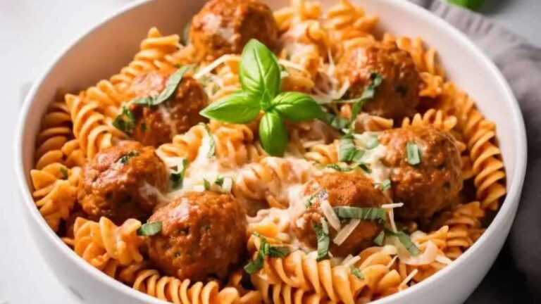 A bowl of pasta with meatballs and basil.