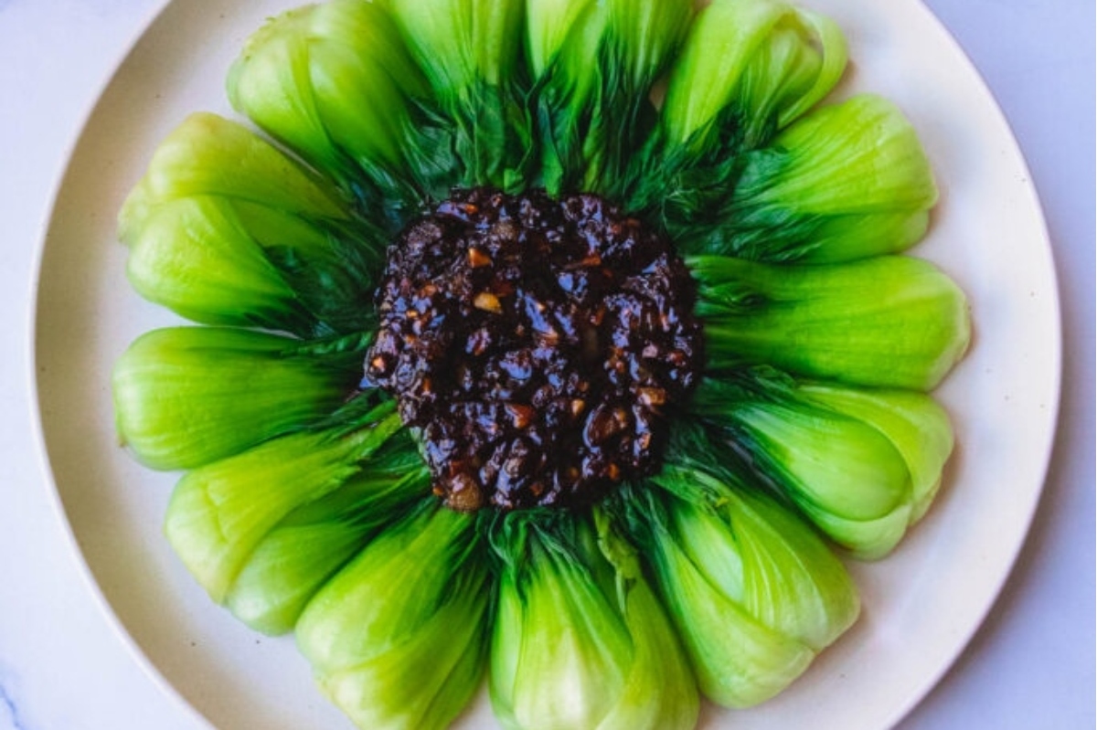 A plate of green chinese cabbage with a sauce on it.