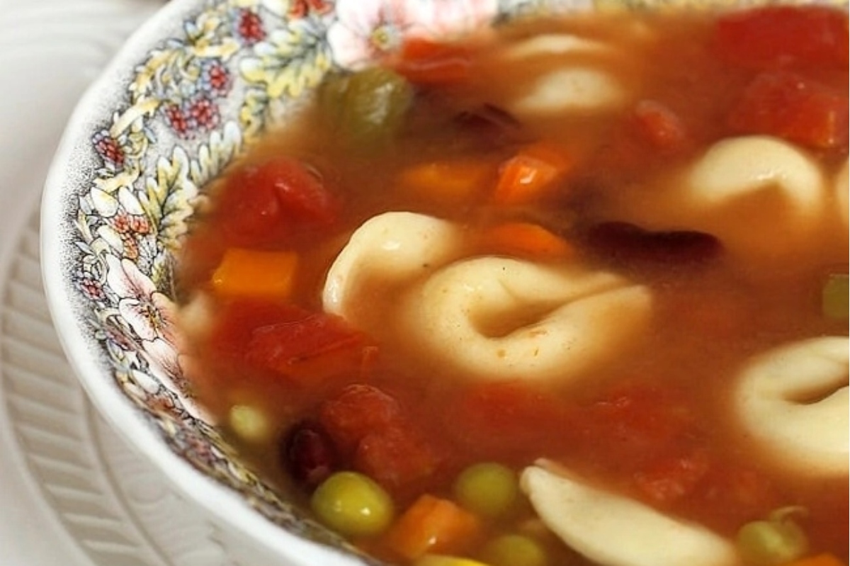A bowl of vegetable soup with tortellini in it.