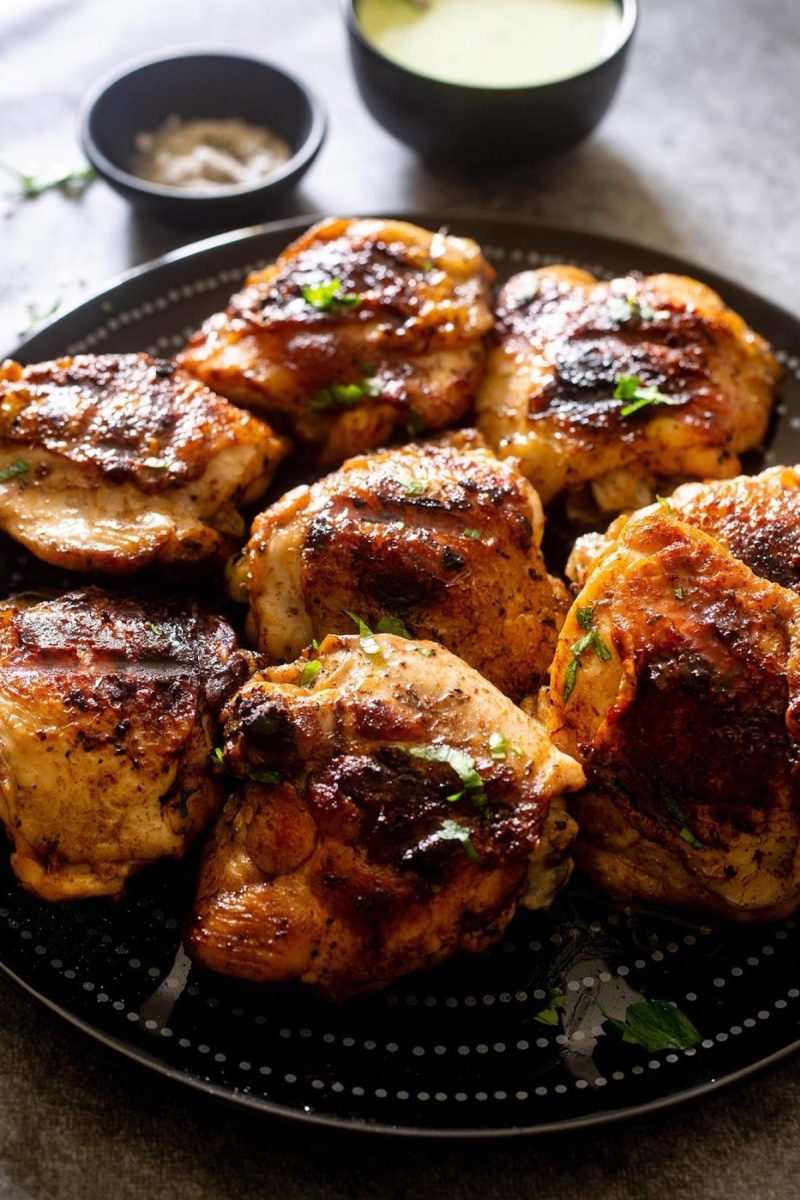 Grilled chicken thighs on a black plate.