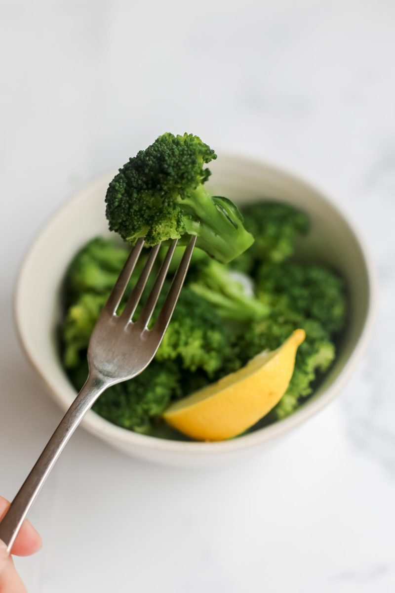 A person holding a fork and broccoli in a bowl.