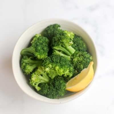 A bowl of broccoli with a slice of lemon.