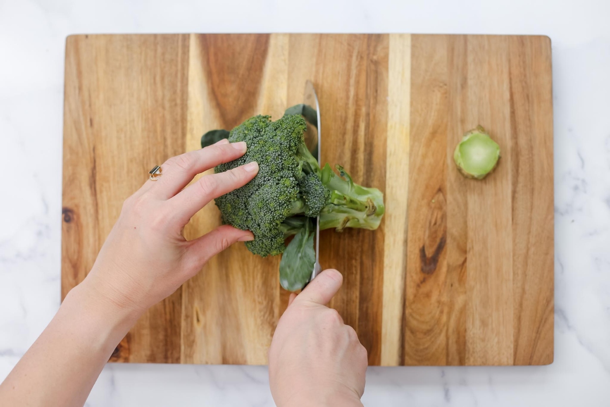A person chopping broccoli on a cutting board.