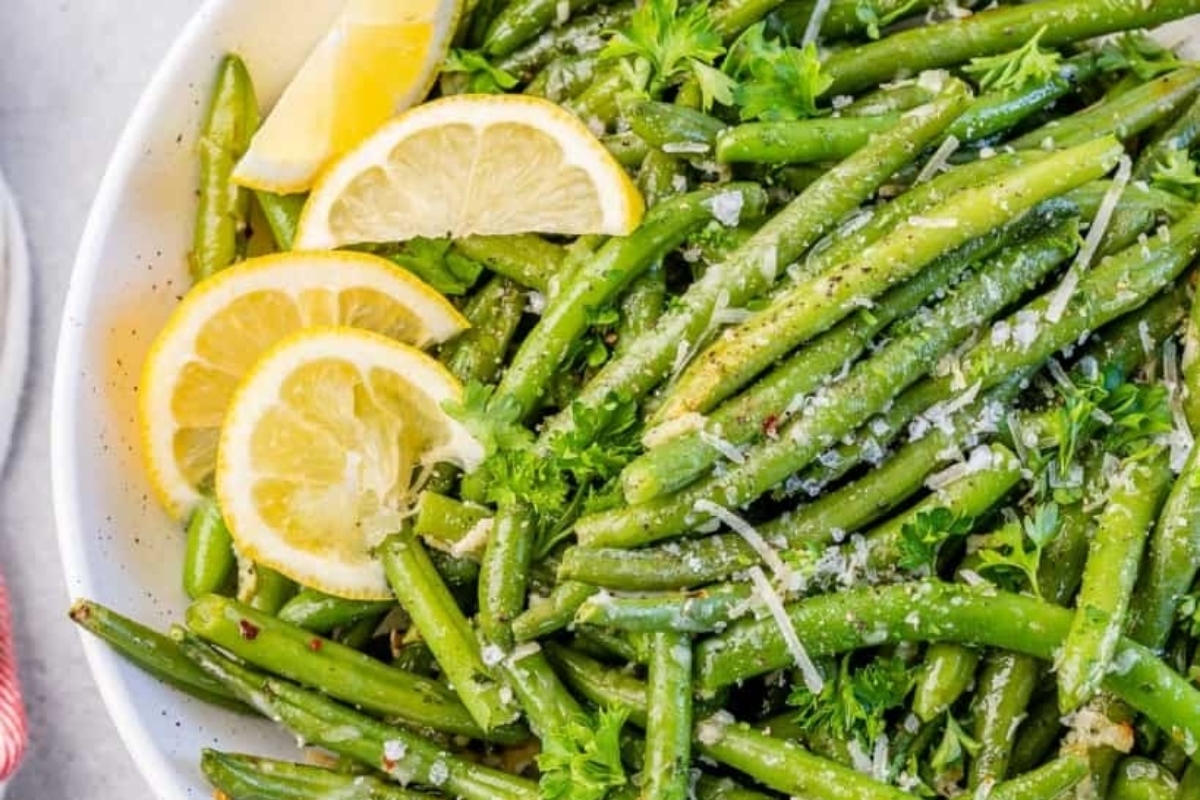 Green beans in a white bowl with lemon wedges.