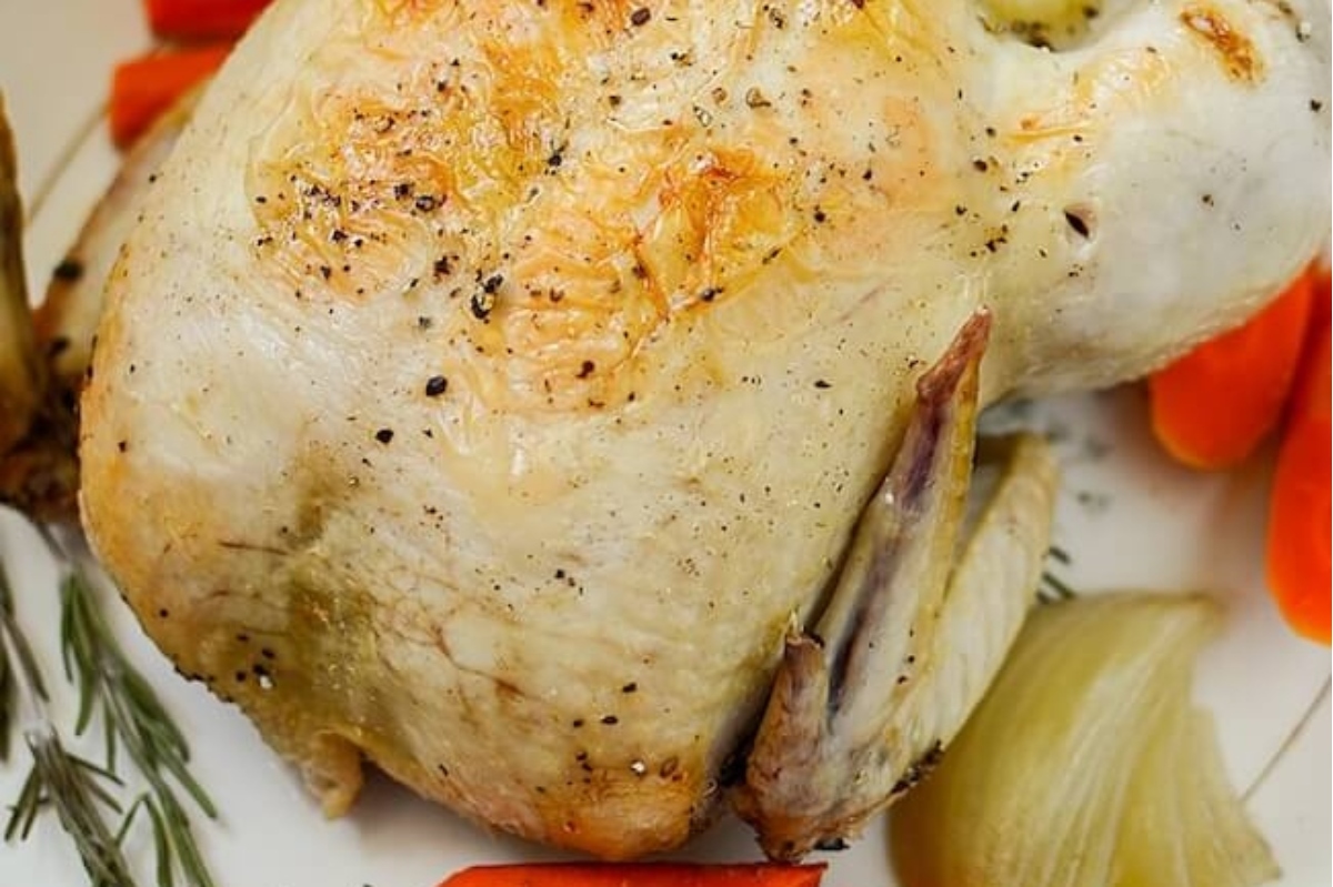A roasted chicken with carrots and onions on a plate.