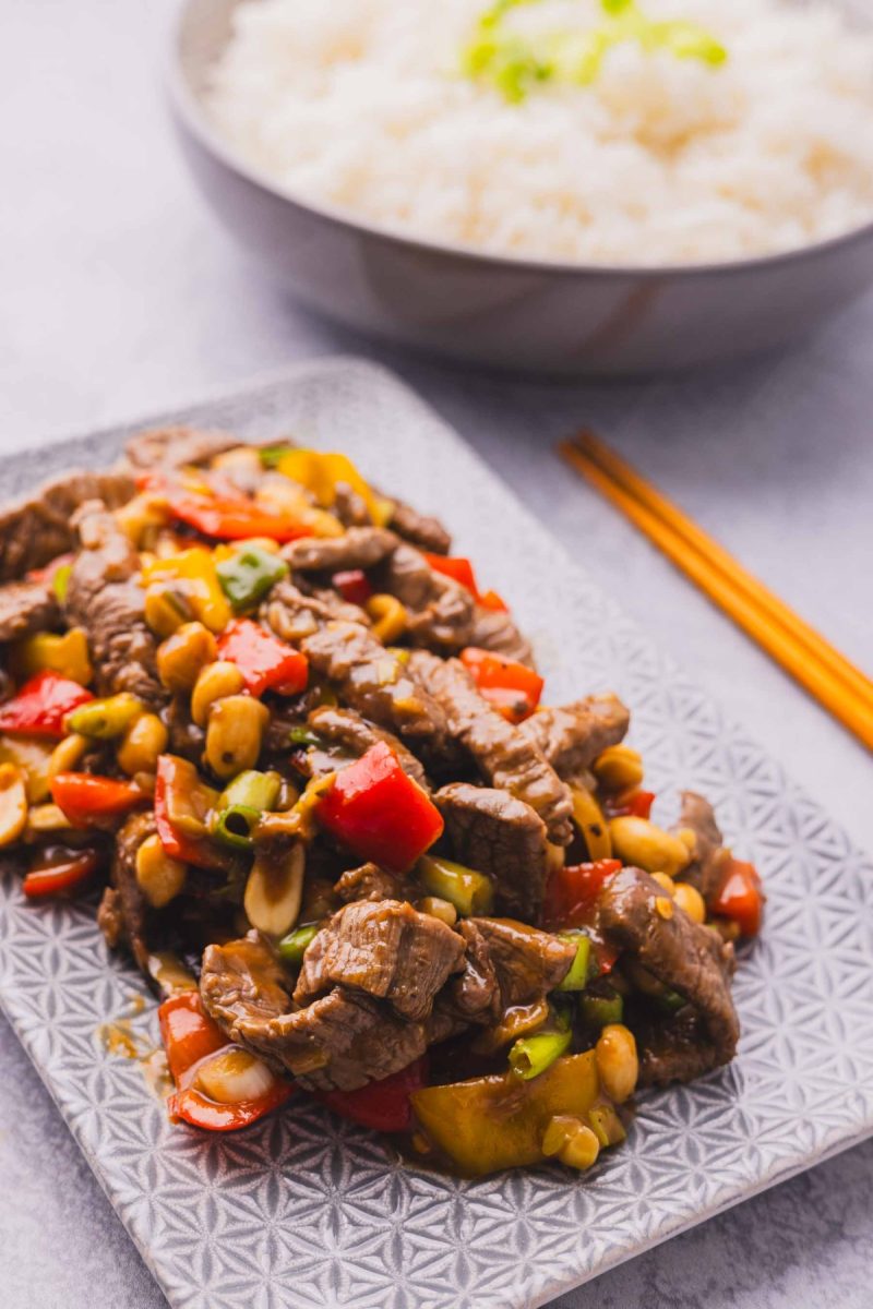 Chinese kung pao beef stir fry on a plate with rice and chopsticks.
