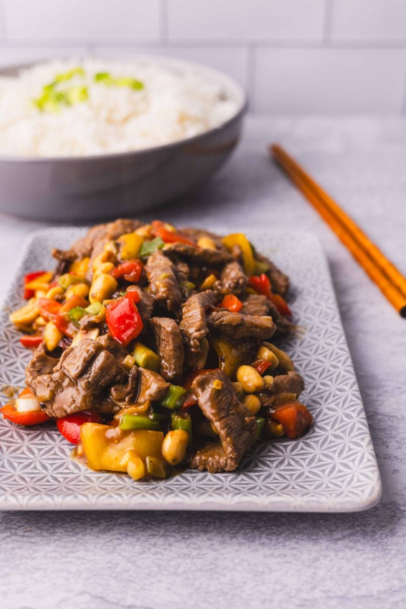 Chinese kung pao beef stir fry on a plate with rice and chopsticks.