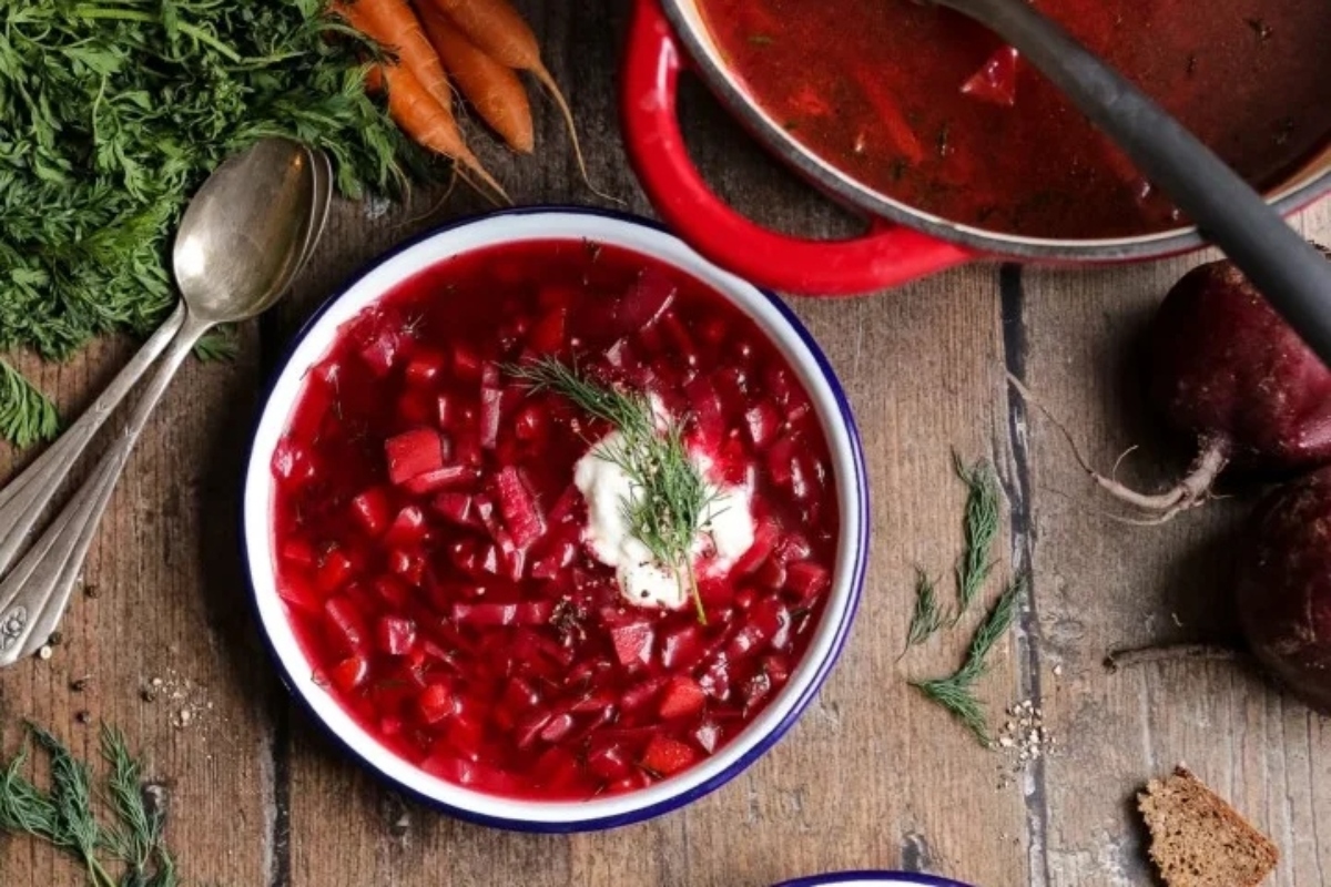 A bowl of beet soup with sour cream and carrots.