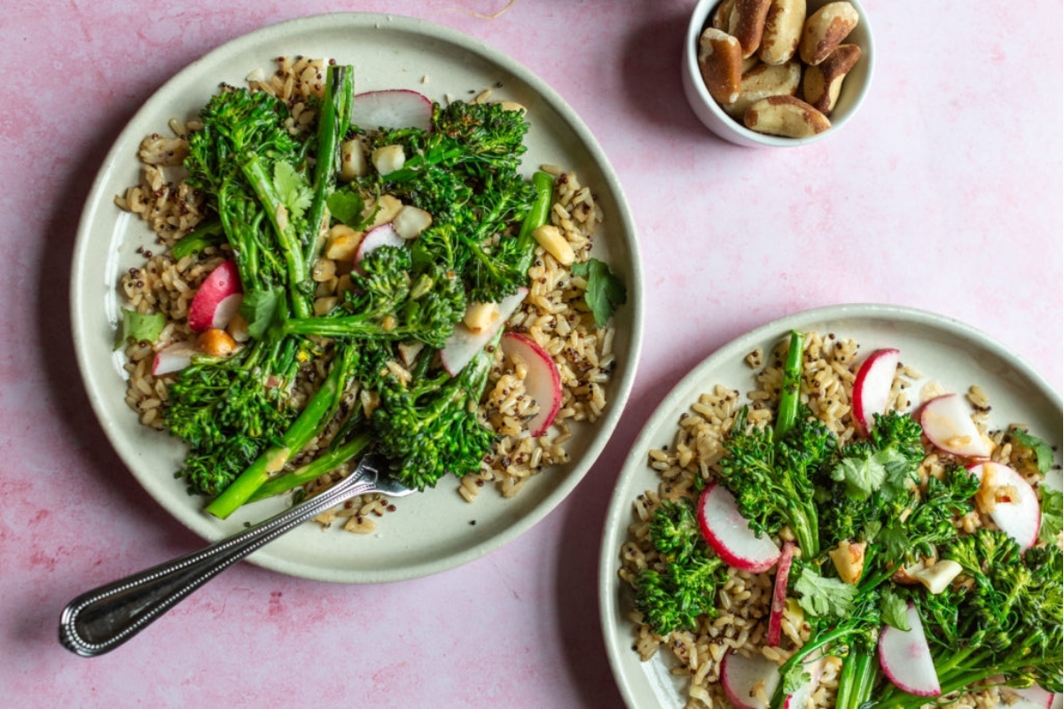 Two plates of broccoli and radishes on a pink background.