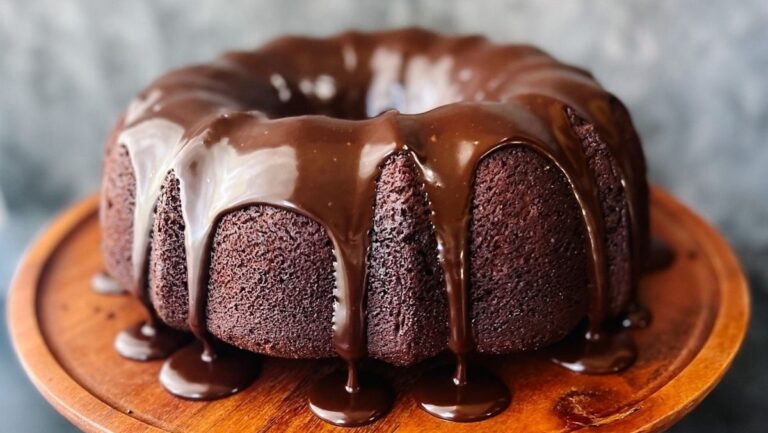 A chocolate bundt cake is sitting on a wooden plate.