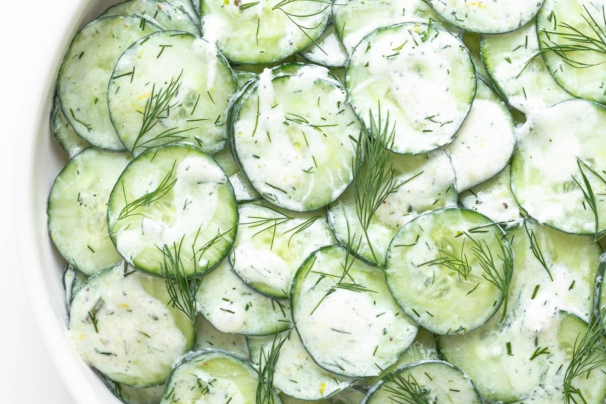 A white bowl filled with cucumbers and dill.