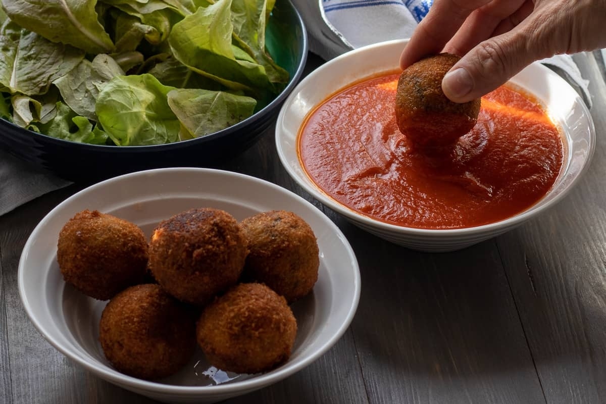A person is dipping meatballs into a sauce.