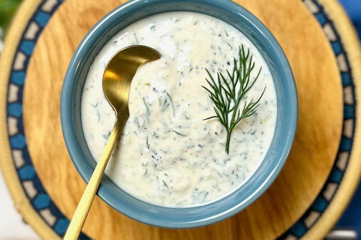 A bowl of lemon dill sauce with a spoon and sprigs of dill.