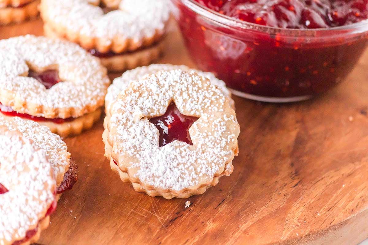 Star-shaped cookies with jam and powdered sugar on a cutting board.