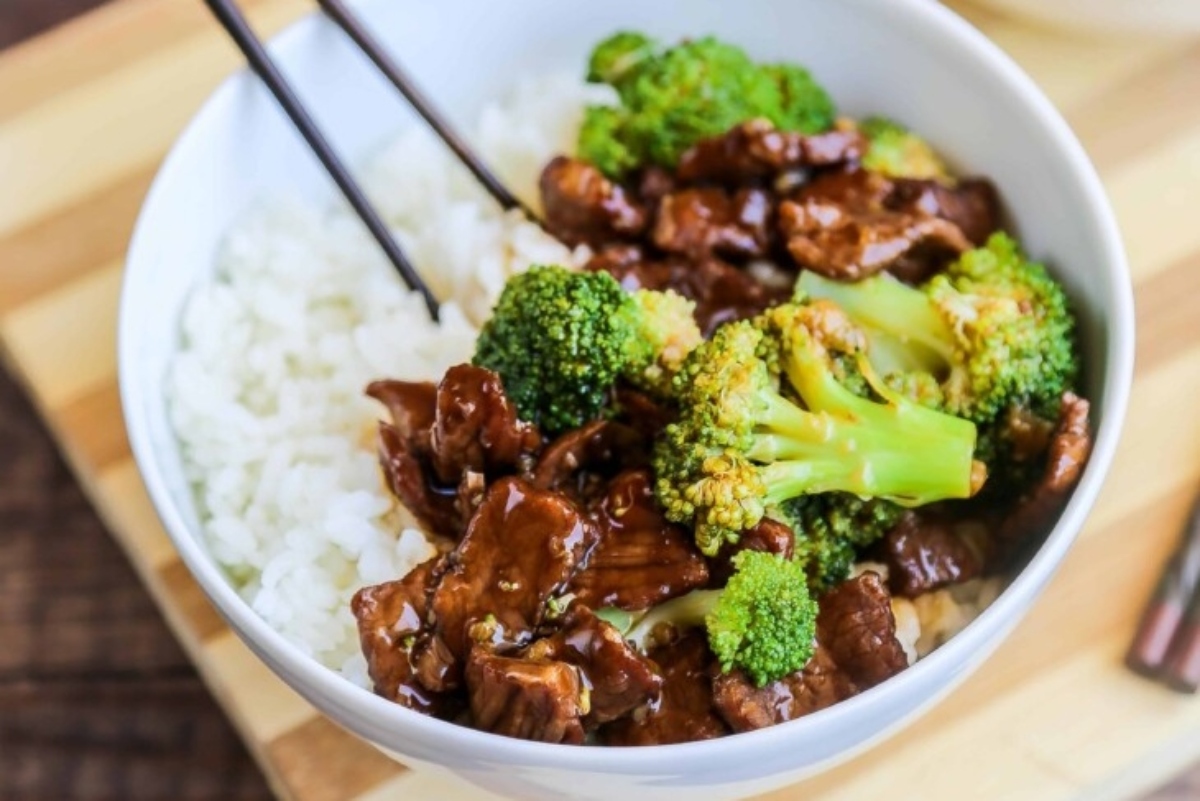 A bowl of beef and broccoli with rice and chopsticks.