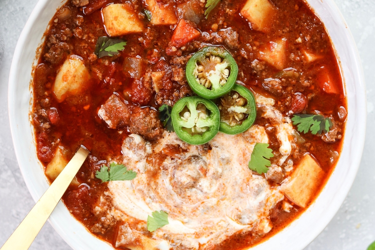 A bowl of chili with cheese and jalapenos.