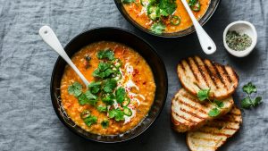 Curried red lentil tomato and coconut soup - delicious vegetarian food on grey background, top view. Flat lay served healthy lunch