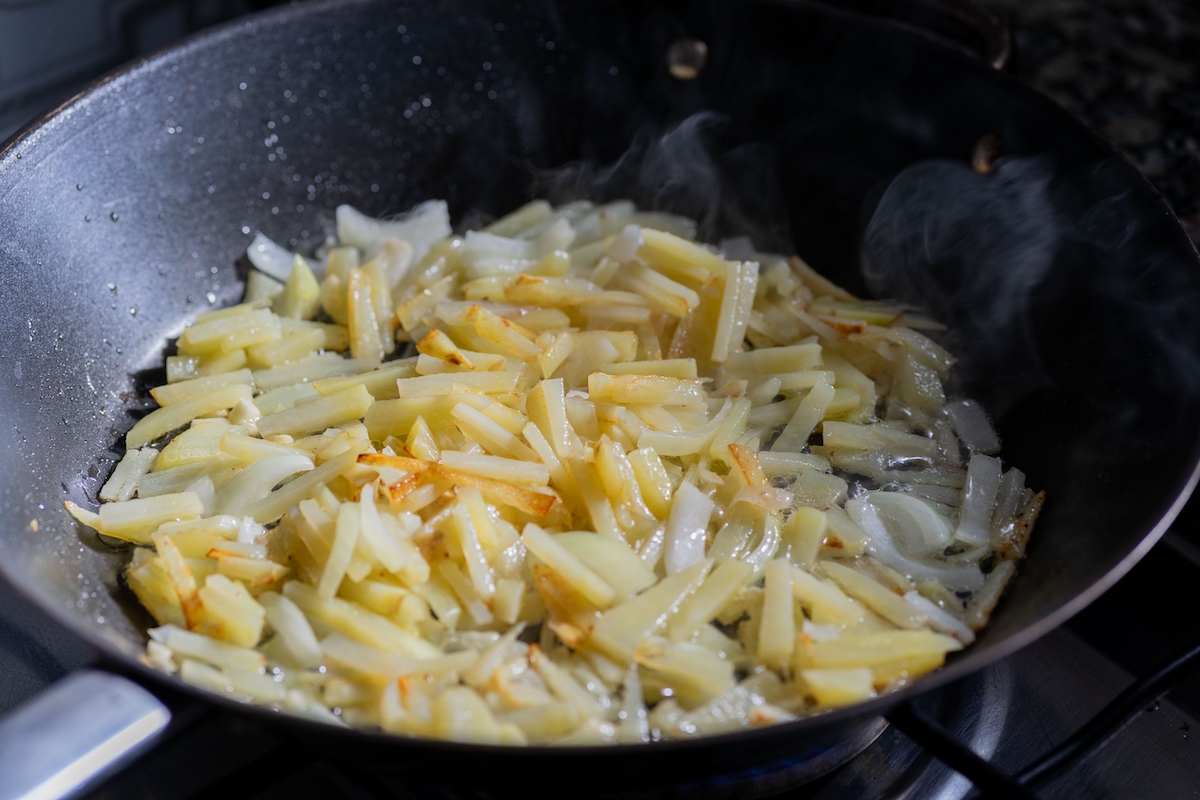 onion and potato cut, frying over vegetable oil in a black frying pan
