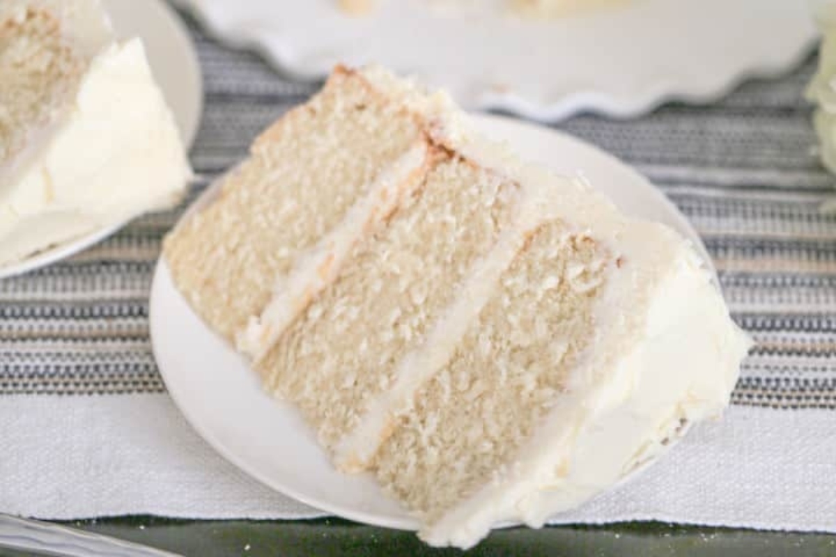 A slice of white cake with frosting on a plate.