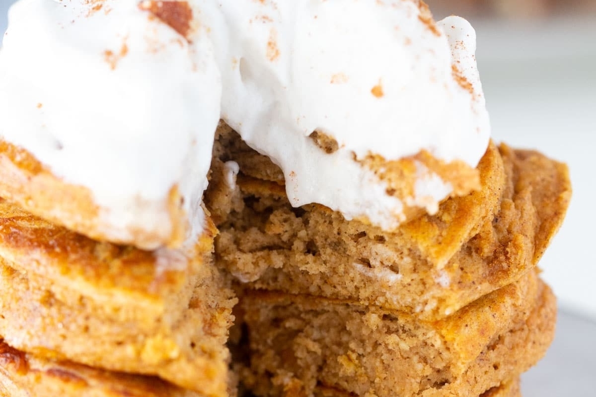 A stack of pumpkin pancakes with whipped cream on top.