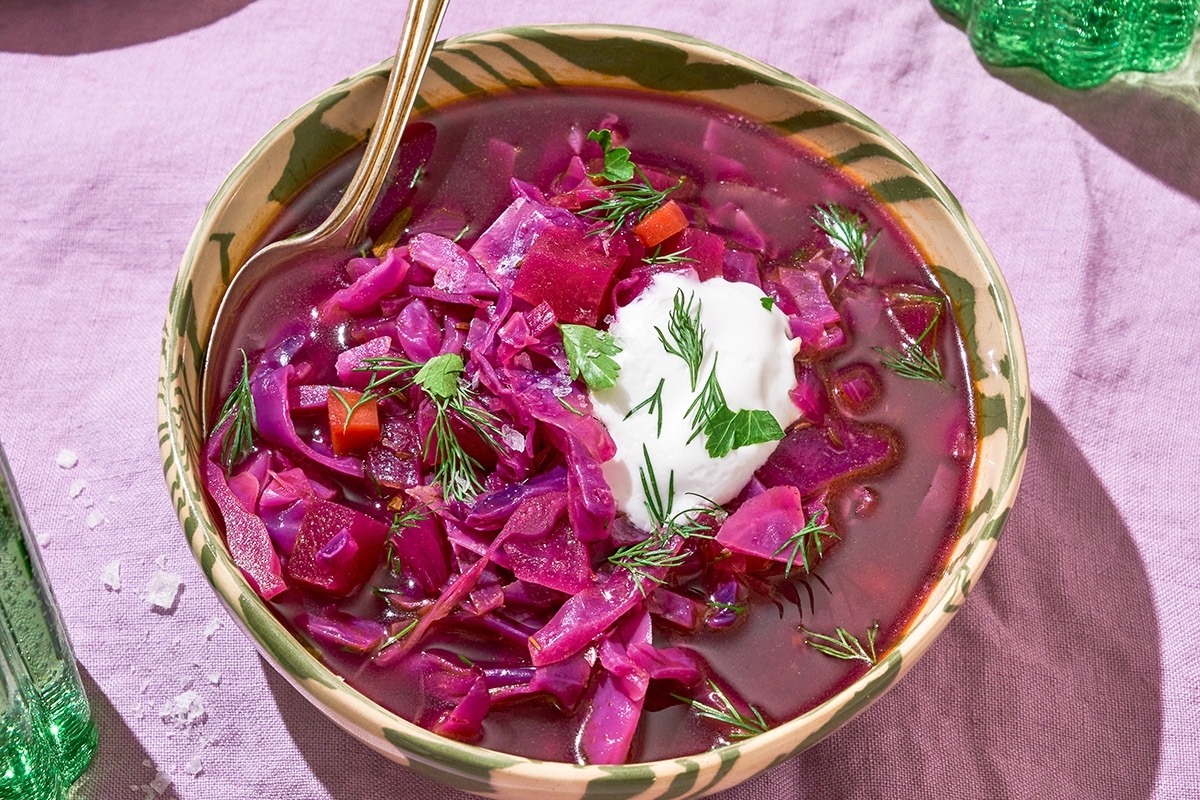 A bowl of red cabbage soup with sour cream.