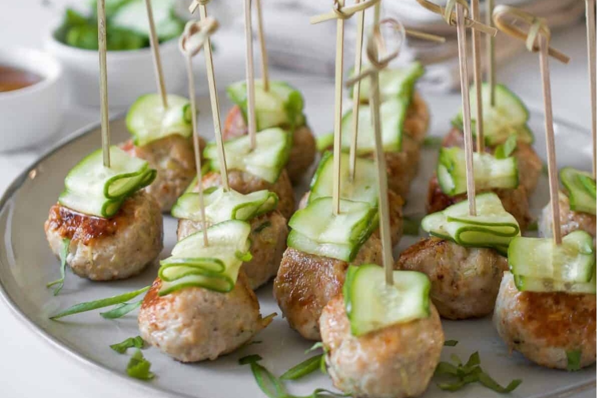 A plate with meatballs and cucumbers on skewers.