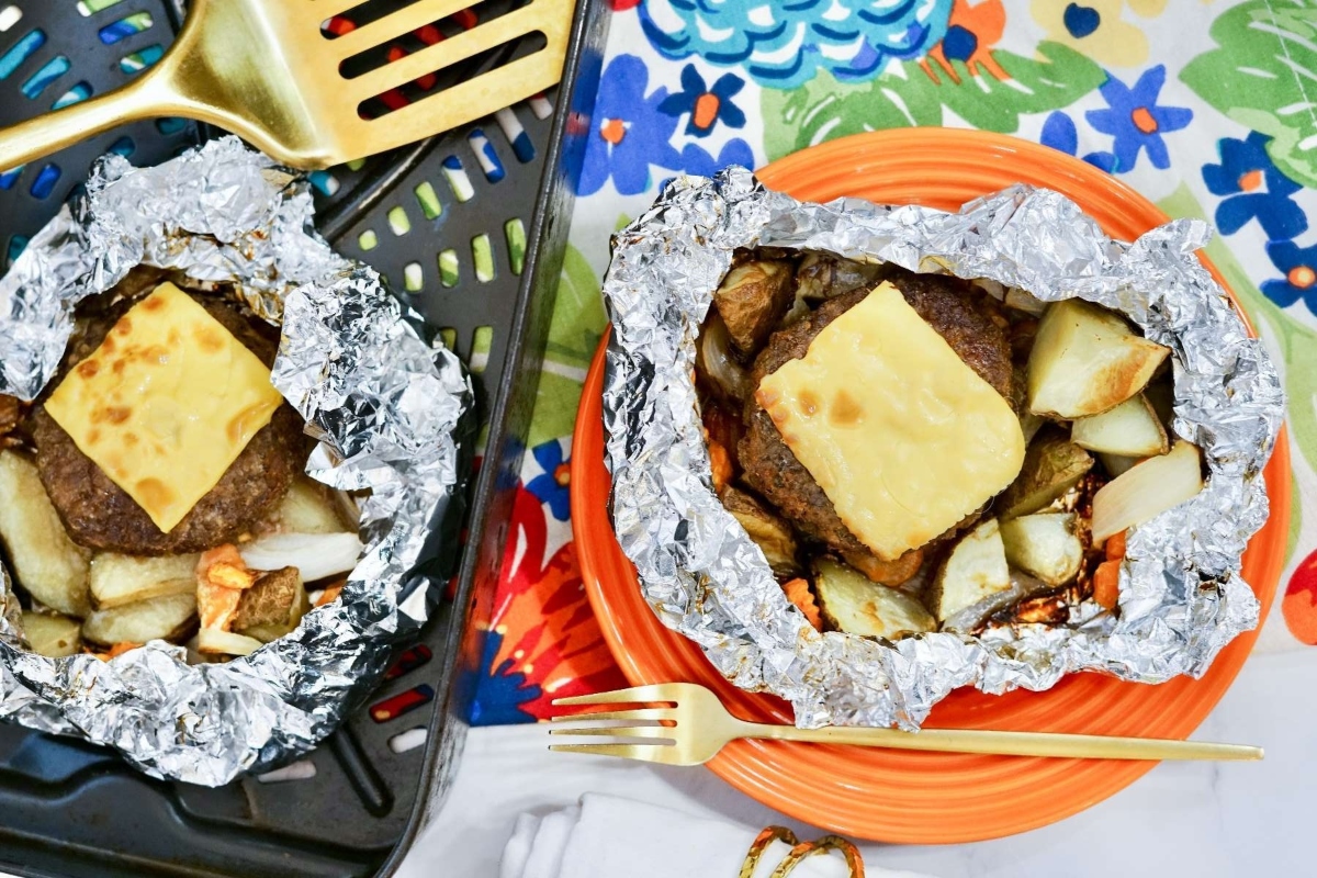 Two foil packets with meat and potatoes on them.